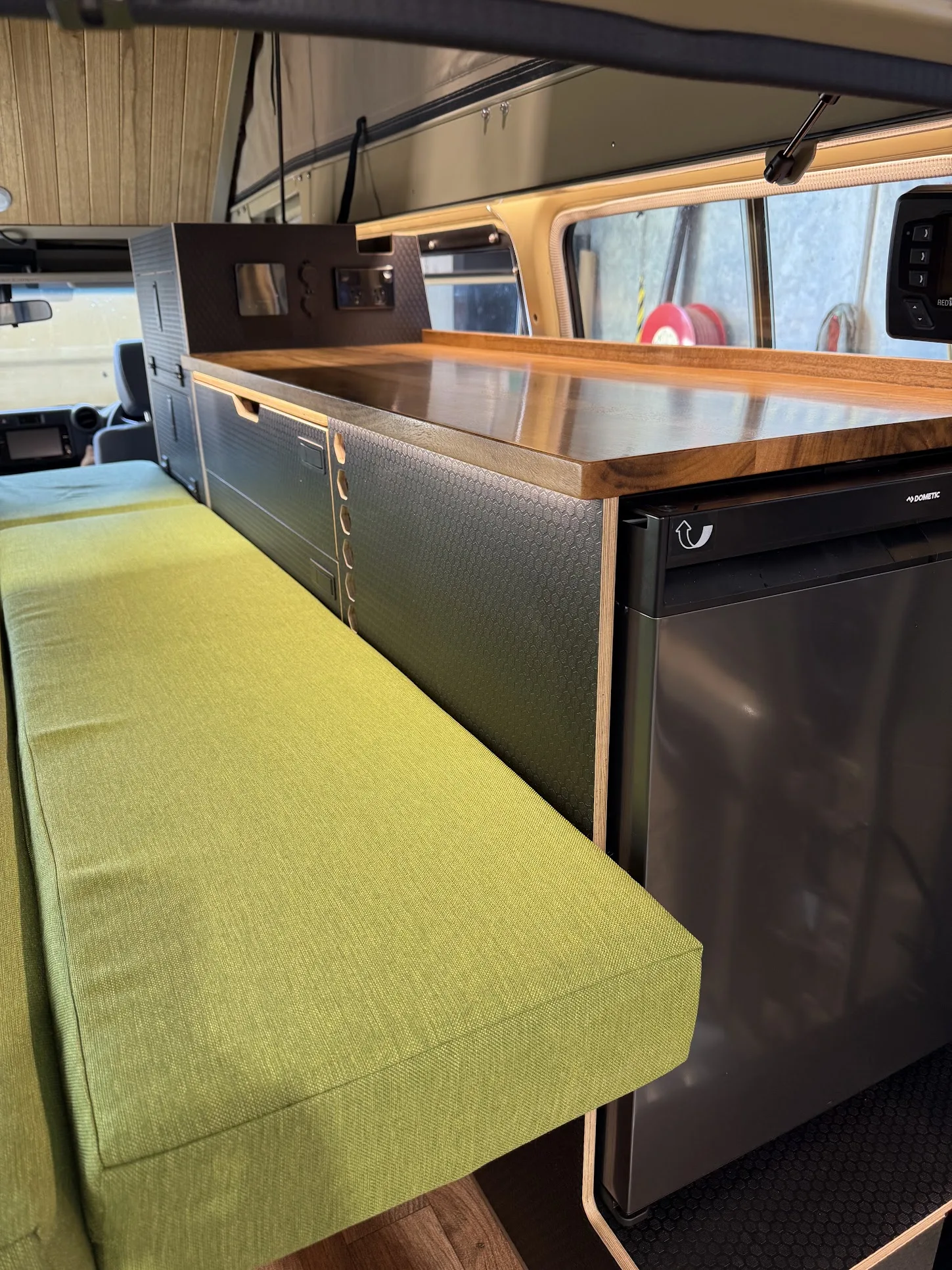 Custom fit-out interior with green bench seat, wooden countertop, and Dometic fridge in a Toyota Land Cruiser Troop Carrier.