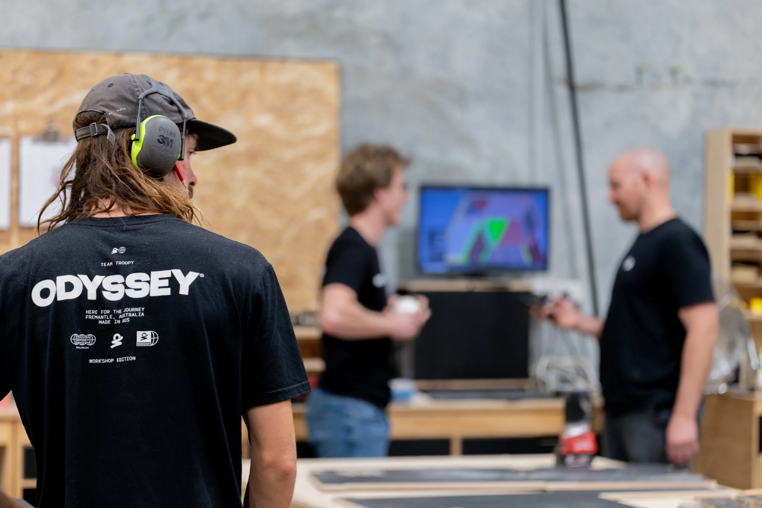Odyssey workshop team members in a warehouse discussing plans on a monitor.